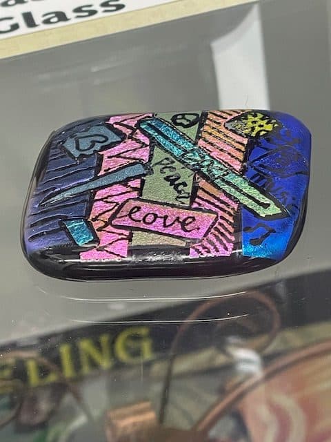 A member's fused dichroic glass pendant reading “Peace Love”